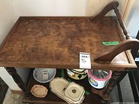 Full view of the wooden tea wagon showing top tray with raised edges, turned legs, bottom shelf with assorted items, and caster wheels.