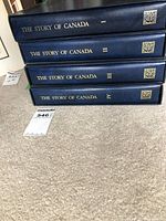Four blue hardcover binders stacked horizontally with gold text reading 'The Story of Canada' Volume I-IV.