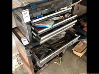 Front view of chest on chest tool cabinet showing three open drawers with various tools inside, cabinet showing rust and wear.
