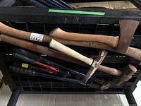 Overview of axes, hammers, pick mattock and mallet with wooden handles, metal heads showing rust and wear, placed on black plastic grid.