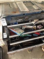 Metal tool chest with drawers partially open showing assorted tools and hand tools inside.