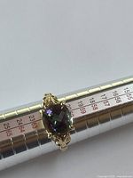 Ring on mandrel showing front angled view of cushion-cut Mystic topaz and ornate gold setting
