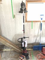 Front view of the entire Troy-Bilt weed eater standing upright in a utility area, showing loop handle and throttle control