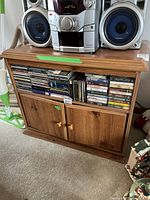 Front view of wood grain media cabinet with stereo system on top and CDs in the open shelf below.