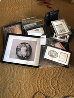 Photo showing variety of picture frames in different sizes and styles, arranged on carpet, including black, white, and gold color frames with some displaying images or art.