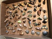 Top-down photo showing about fifty small ceramic animal figurines arranged in a box, various species and natural colors.