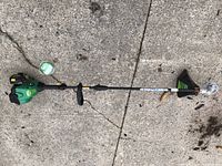 Full view of WeedEater FeatherLite SST25CE string trimmer lying on concrete with included trimmer line spool nearby.