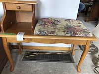 Full view of wood bench with natural finish featuring floral upholstered cushion and integrated table with drawer on side.