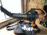 Side view of the Worx WG500 electric leaf blower with attached collection bag. Shows the elongated nozzle, handle, and bag connections.