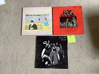 Photo showing front covers of three Alice Cooper vinyl records: 'Pretties For You' (purple illustrated cover), 'Easy Action' (red cover with band photo), and a black and white photo album cover.