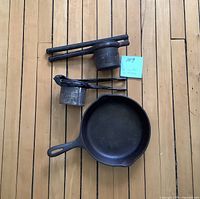 Photo shows two heavy steel potato ricers and one cast iron skillet on wooden floor.