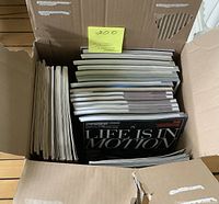Photo showing a heavy cardboard box filled with a large stack of automotive magazines and programs, viewed from above.