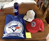 Blue Jays XL blue t-shirt with circular 40th season logo, two Blue Jays hats (gray/black and red), blue metallic water bottle with Blue Jays logo.
