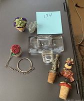 All six bottle stoppers displayed on flat surface showing various decorative tops, including metal rose with chain, male soldier figure, clear glass stoppers, and flower basket designs.