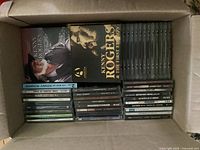 Top-down view of a cardboard box filled with CD albums, mainly country music and Christmas themes, including Kenny Rogers albums packed neatly.