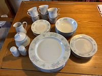 Full view of all dishes including plates, bowls, cups with saucers, cream, sugar, and salt & pepper shakers, arranged on wooden table