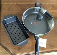 Image of the covered frying pan with glass lid and the meat loaf pan with perforated insert on a wooden table.