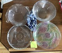 Overview of two large glass bowls, two glass serving plates, and four patterned cotton napkins with blue napkin rings arranged on a wooden table.