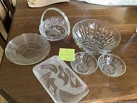 Photo showing all the items together on a wooden table: large clear glass bowl, two smaller matching bowls, frosted rectangular plate, clear circular plate, and clear glass brides basket.