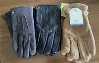 Photo shows three pairs of gloves: grey wool blend with buttons, black leather gloves, and beige fleece gloves with size tag.