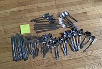 Whole lot of cutlery pieces laid out showing different types of cutlery in two incomplete sets.