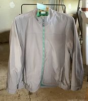 Front view of men's light grey jacket with green fleece lining, zippered front and stand collar