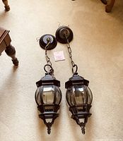 Pair of dark rubbed bronze indoor pendant lights with curved glass panels laid on carpet showing top ceiling mounts, chains, and fixture design.