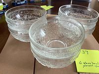Three clear pressed glass bowls showing embossed floral pattern and dot bands around the outside edges.