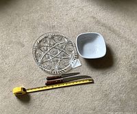Clear pressed glass plate next to white ceramic bowl and two carving knives with wooden handles, measuring tape included for size reference.