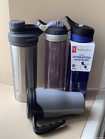 Four refillable water bottles; one stainless steel, two Contigo plastic bottles, and one blue President's Choice plastic bottle with push-button spout.