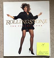 Front cover of Rolling Stone The Photographs large soft cover book showing a woman jumping in black dress and fishnet stockings with title text in gold and red.