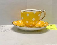 Side view of the yellow polka dot tea cup on matching saucer, showing bright colors and gold trim.