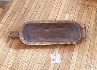 Top view of the rustic wooden trug showing the deep carved bowl and handle, placed on wooden floorboards with a small sign showing "103" and dimensions 25 x 9.
