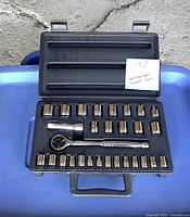 Open black carrying case showing chrome sockets and ratchet wrench neatly arranged. Note with item details visible.