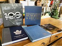 Five large hardcover sports and hockey related commemorative books arranged on a wooden table including NHL 100th Anniversary and Maple Leaf Gardens volumes.