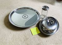Set of steel kitchen items including lazy Susan, covered dish, and sugar dispenser arranged on carpet