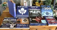 Photo showing multiple Toronto Maple Leafs books stacked on a table, titles include 'We Are Your Leafs,' 'Leafs '66,' 'Maple Leafs Top 100,' and others.