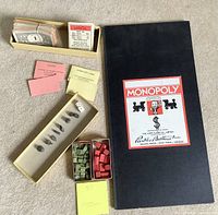 Vintage Monopoly game components spread including the game board, cards, game money, houses, metal pieces, and dice.