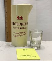 Front and side view of the ceramic water jug with Whyte & Mackay Scotch Whisky branding and the thick glass shot measurer next to it, with a ruler for scale.