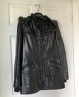 Front view of black leather Danier women's winter jacket with zip and snap button closures, removable hood with fur trim, and multiple pockets.