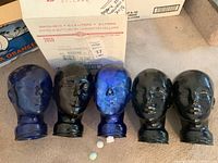Five glass display heads in blue and black on a carpeted surface with cardboard boxes in background.