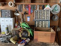 Wide view of many tools and hardware items against a pegboard including Black & Decker drill, jigsaw, cord reel, plastic organizers with small parts, and extension cords.