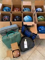 Nine variously colored swirl-pattern bowling balls in cardboard boxes and four bowling bags arranged on floor