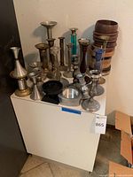 Photo of all candlesticks and bowls grouped on white surface against wall.