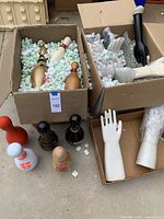 Various decorative bowling pins in two cardboard boxes with packing peanuts, including wood and ceramic with multiple color patterns.