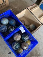 Blue crates filled with multiple small bowling balls showing varied marbled color patterns and surface wear.