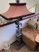 Full side view of floor lamp showing pink fabric shade with fringe and decorative black stepped base with brass pole.