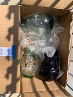 Top view of four glass mannequin heads placed inside a cardboard box with bubble wrap, showing different glass styles including clear and black glass heads.