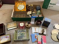 Full view of jewelry boxes, decorative coasters and small framed items arranged on floor in a cardboard box and around it.