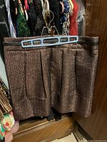 Metallic bronze pleated skirt with waistband detail hanging on blue hanger in closet with other clothing.